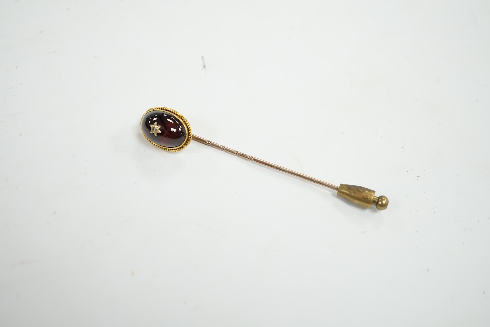 A cased Victorian yellow metal, oval cabochon garnet and diamond chip set stick pin, overall 77mm. Condition - fair